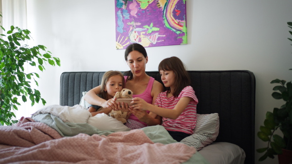 Portrait of a mother with two daughters on a bed in the bedroom. Fatherless family sit and hug each other. Concept of Mother's Day and maternal love.