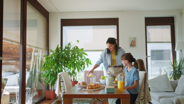 Mother prepares breakfast and pouring juice for the children, in the morning. Maternal love and care for the household and family.