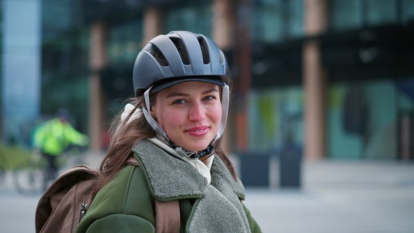 A young urban woman traveling around the city by bike, cycling to work, university to save money. Woman with a cycling helmet standing by bicycle. Concept of bike commuting in the city, sustainable lifestyle.