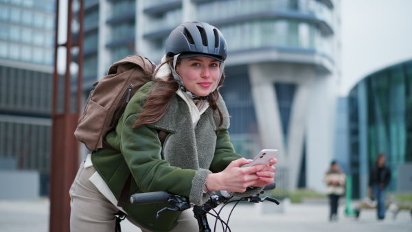 A young urban woman traveling around the city by bike, cycling to work, university to save money. Woman with a cycling helmet standing by bicycle. Concept of bike commuting in the city, sustainable lifestyle.