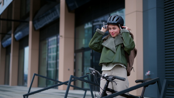 Video of beautiful urban woman putting cycling helmet on head. Bike rack in front of office building, university. Concept of bike commuting in the city, sustainable lifestyle.