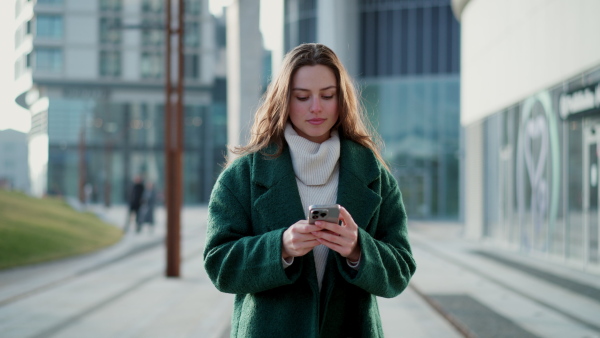 Video of beautiful young woman in the city, scrolling on smartphone, text messaging. Fashionable Gen z woman smiling, looking at smartphone.