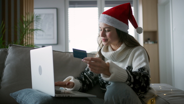 A beautiful woman in santa hat shopping online, paying with credit card.