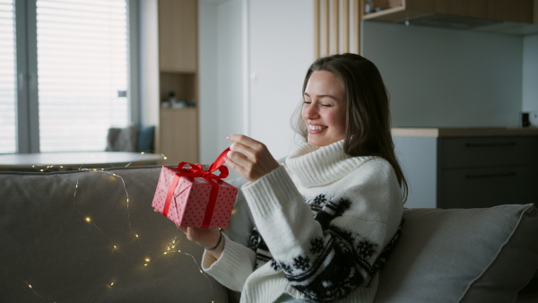 A beautiful woman holding a wrapped gift in her hand, opening it and smiling. A Christmas surprise or birthday gift from a friend delivered by mail.