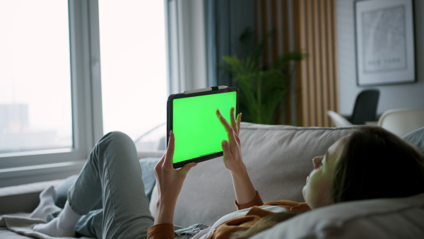 A woman with tablet laying on sofa wiht tablet with green screen.