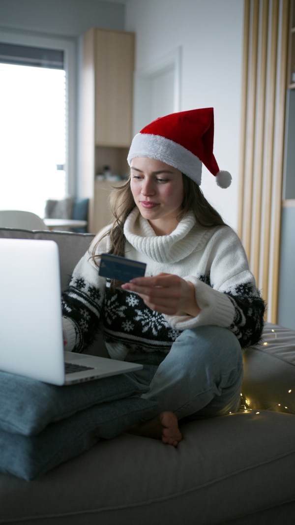 A beautiful woman in santa hat shopping online, paying with credit card.