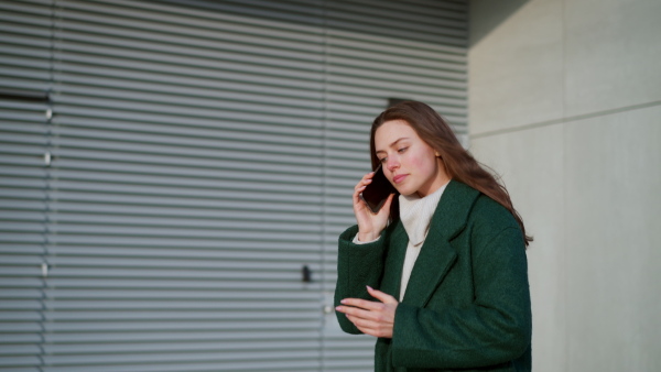 A beautiful young woman making phone call, walking on city street. Female university student in front of university building.