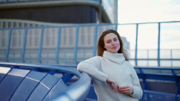 Video of beautiful young woman in the city. Standing on city street, university student in front of university building. Fashionable Gen z woman smiling, looking at camera.