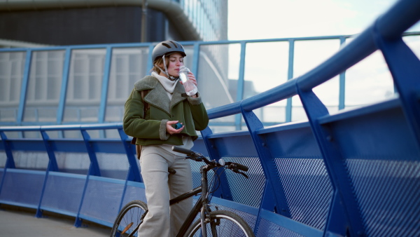 A young urban woman traveling around the city by bike, stopping to drink water. Concept of bike commuting in the city, sustainable lifestyle.