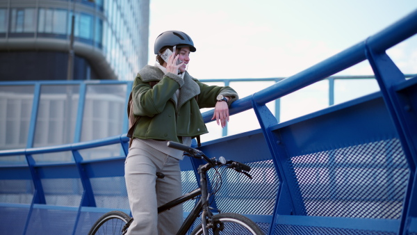 A young urban woman traveling around the city by bike, stopping to make phone call on smartphone. Concept of bike commuting in the city, sustainable lifestyle.