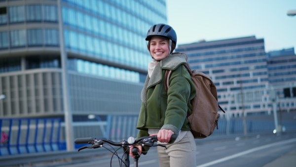 A young urban woman traveling around the city by bike, cycling to work, university to save money. Woman with a cycling helmet standing by bicycle. Concept of bike commuting in the city, sustainable lifestyle.