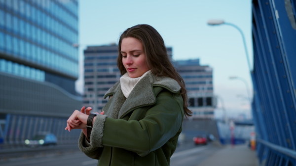 Video of beautiful young woman in the city. Standing on city street, using smartwatch. Fashionable Gen z woman smiling.