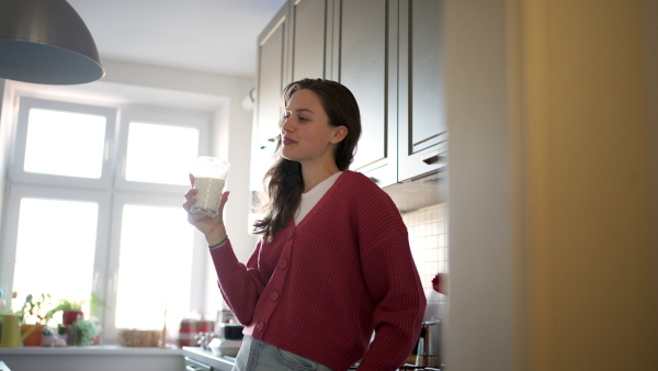 Beautiful woman drinking a glass of plant-based milk in the kitchen.