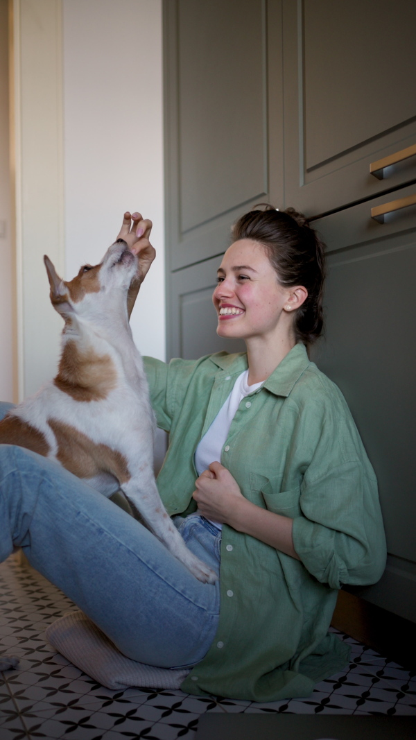 Beautiful single woman sitting on floor, playing with her dog. Young woman living alone in apartment, enjoying weekend.