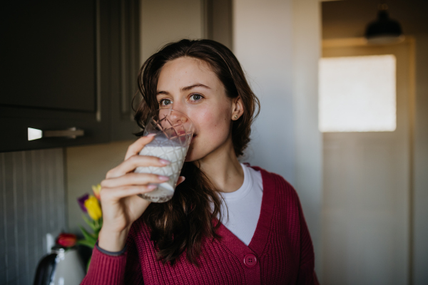 Beautiful woman drinking a glass of plant-based milk in the kitchen.