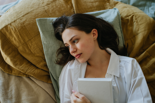 Top view of woman thinking about book in bed, cozy and contented feeling, finished story. Freedom, weekend activity for single woman.