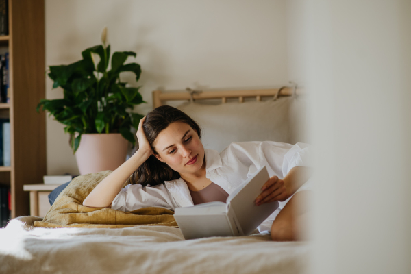 Beautiful woman reading book in bed, cozy feeling. Freedom, weekend activity for single woman.