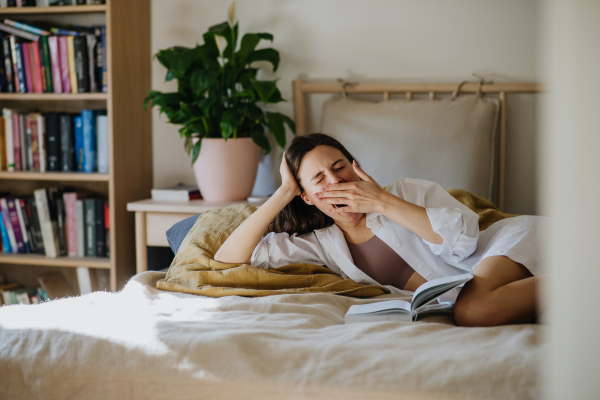 Beautiful woman yawning, reading book in bed, cozy feeling. Freedom, weekend activity for single woman.