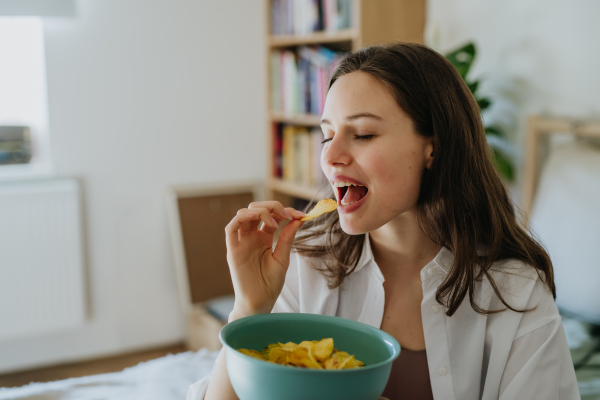 Enjoying crunchy chips. Woman has cravings for potato chips, eating with closed eyes, holding bowl full of crisps.