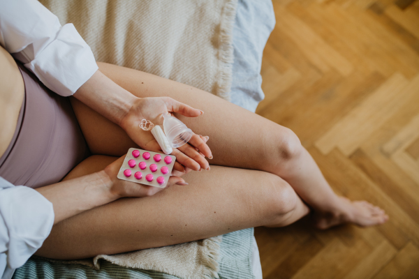 Young woman at home suffering from menstrual pain, having cramps. Woman warming lower abdomen with a hot water bottle, endometriosis, and conditions causing pain in tummy.