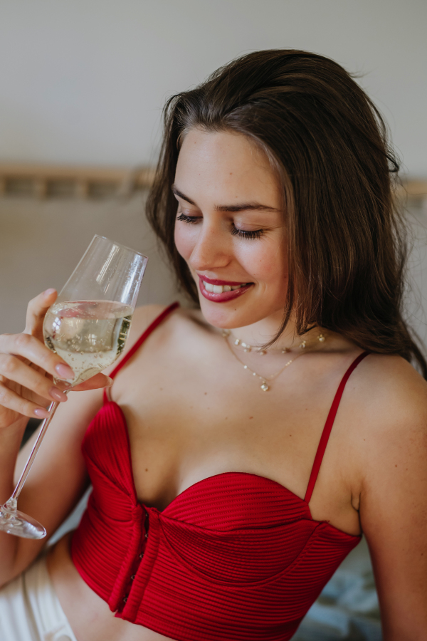 Romantic woman drinking champagne from a glass, dressed in a red attractive corset. Concept of Valentine's Day, love and romantic relationship.