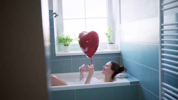 Young attractive woman enjoying bath, playing with heart-shaped balloon. Valentines concept.