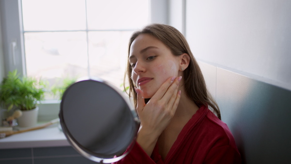 Beautiful woman applying moisturizing body lotion on her skin, legs. Skincare, beauty routine. Woman sitting in the bathroom on the bathtub, dressed in a bathrobe. Close up on leg.