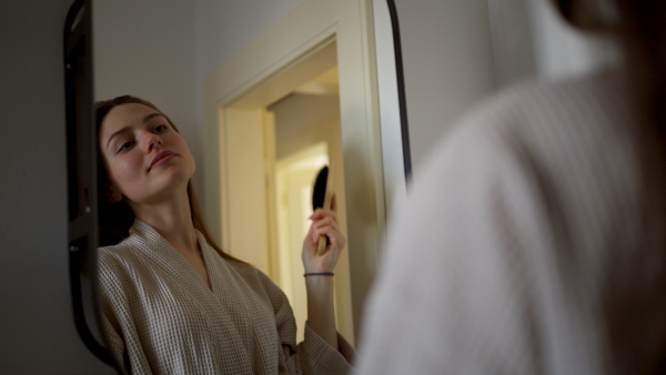 Young woman standing in front of the mirror and doing her haircare routine. Preparing to go outside.