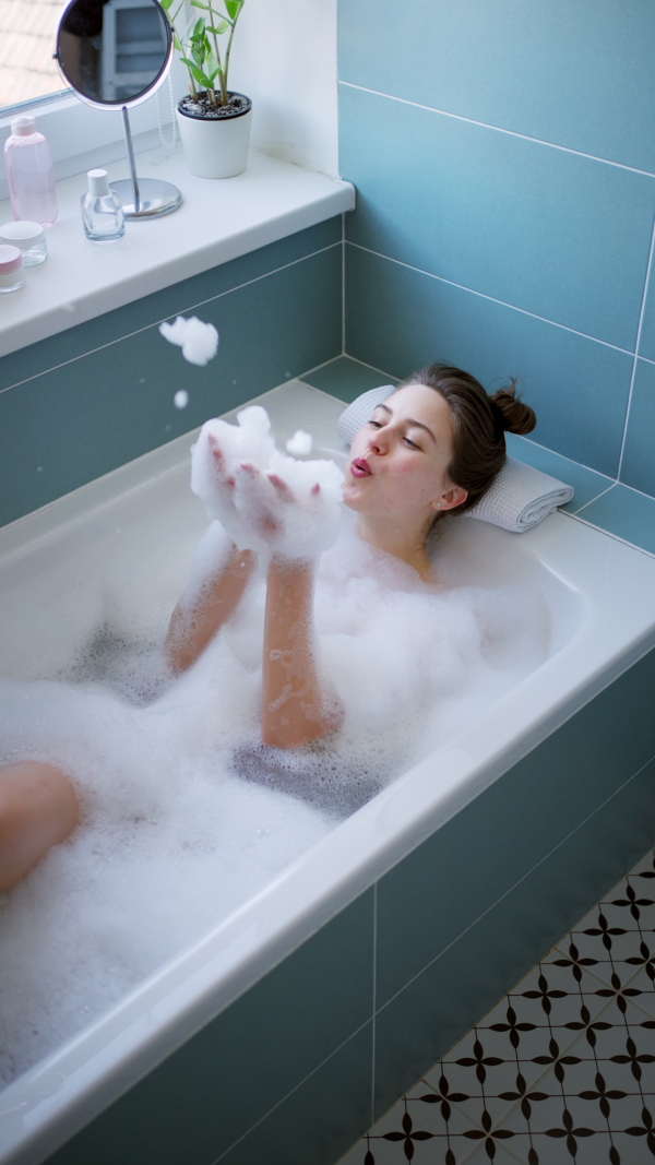 Young attractive woman enjoying bath, blowing bubbles.