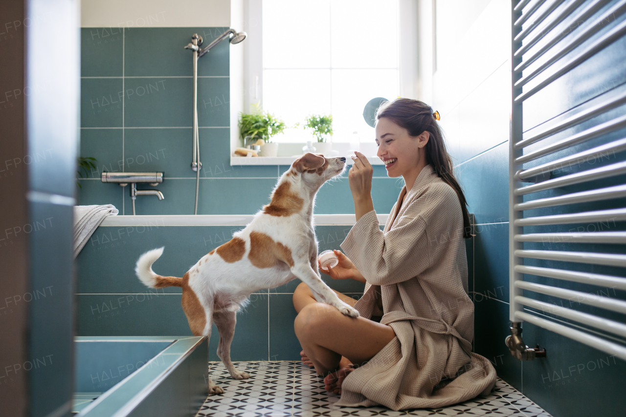 Young woman playing with a dog in the bathroom, getting ready for a bath in the tub. Relax after long work day.