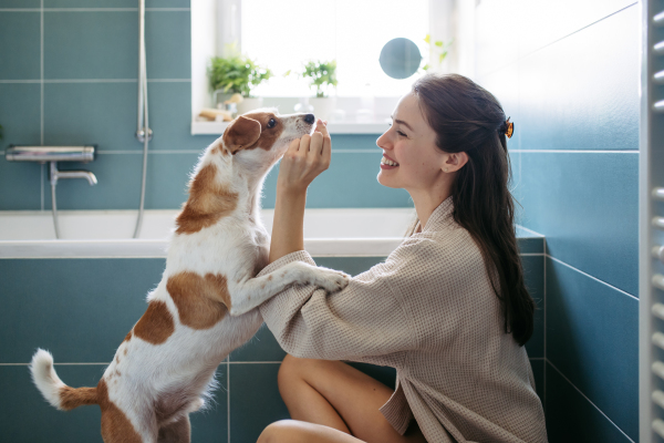 Young woman playing with a dog in the bathroom, getting ready for a bath in the tub. Relax after long work day.