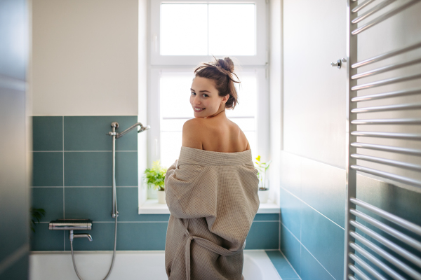 Beautiful woman getting ready for a bath in the bathtub, relaxation in hot water after a long day. Taking off her robe.