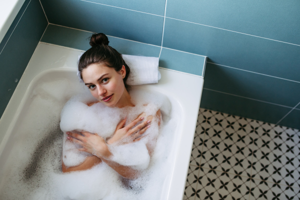 Top view of beautiful woman relaxing in warm bathwater, soaking in bathtub. Enjoying bubble bath, smiling, looking at camera.