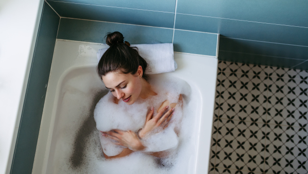 Top view of beautiful woman relaxing in warm bathwater, soaking in bathtub. Enjoying bubble bath and smiling.