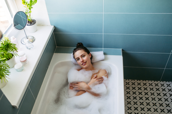 Top view of beautiful woman relaxing in warm bathwater, soaking in bathtub. Enjoying bubble bath, smiling, looking at camera.