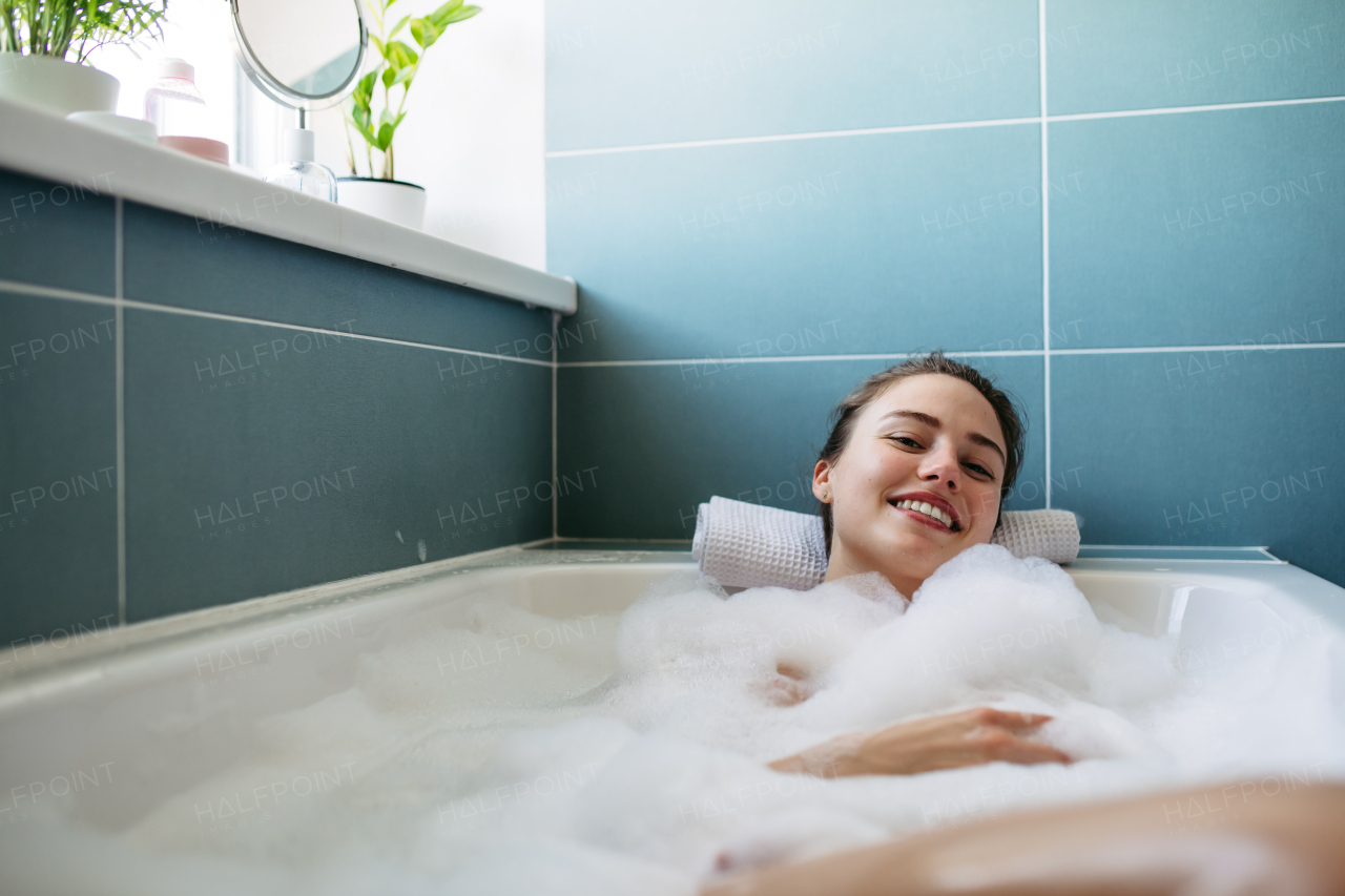 Beautiful woman relaxing in warm bathwater, soaking in bathtub. Enjoying bubble bath, smiling, looking at camera.