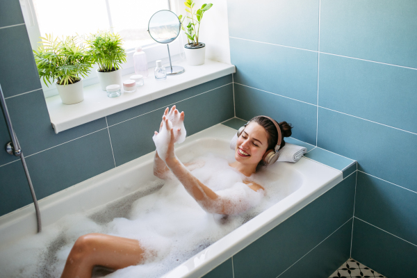 Beautiful woman relaxing in bathtub, listening music through headphones while soaking in hot water. Enjoying a bubble bath with music.