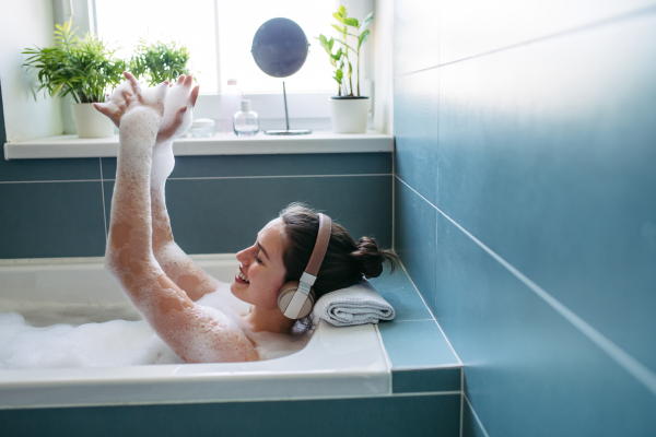 Beautiful woman relaxing in bathtub, listening music through headphones while soaking in hot water. Enjoying a bubble bath with music.