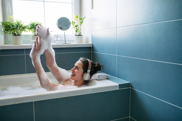 Beautiful woman relaxing in bathtub, listening music through headphones while soaking in hot water. Enjoying a bubble bath with music.