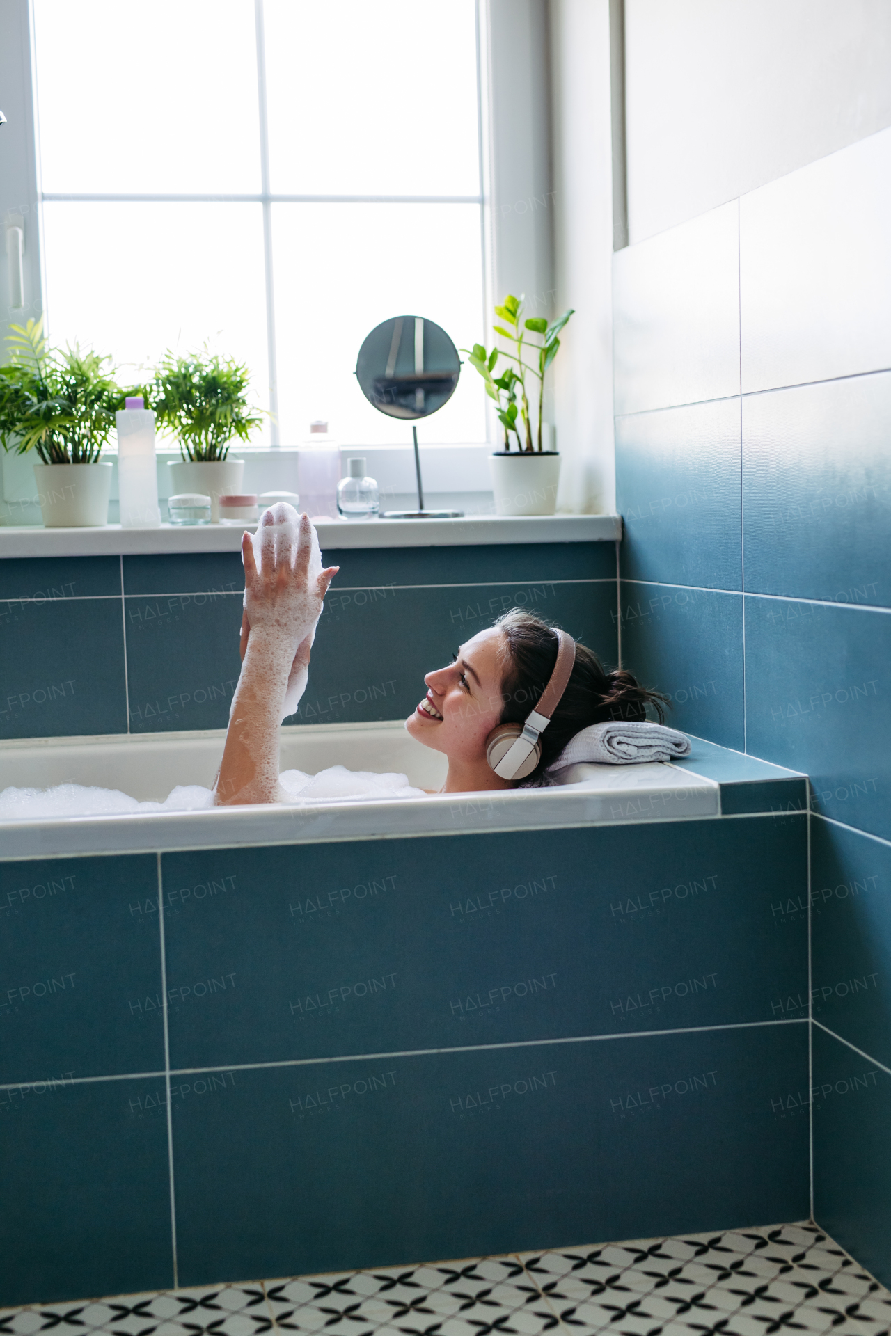 Beautiful woman relaxing in bathtub, listening music through headphones while soaking in hot water. Enjoying a bubble bath with music.