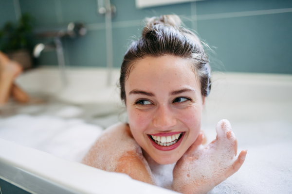 Beautiful young woman lying in bathtub, soaking in warm water. Enjoying a bubble bath, smiling, having fun.