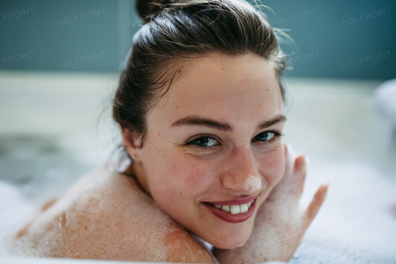 Portrait of beautiful young woman lying in bathtub, soaking in warm water. Enjoying a bubble bath, smiling, having fun.