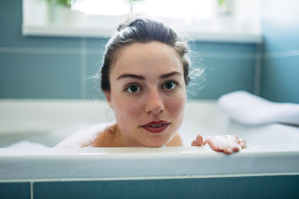 Portrait of beautiful young woman lying in bathtub, soaking in warm water. Enjoying a bubble bath, relaxing.