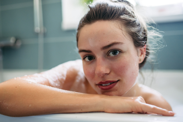 Portrait of beautiful young woman lying in bathtub, soaking in warm water. Enjoying a bubble bath, smiling, having fun.