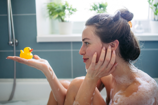 Beautiful young woman in bathtub with rubber duck in hand. Enjoying a bubble bath, smiling, having fun.