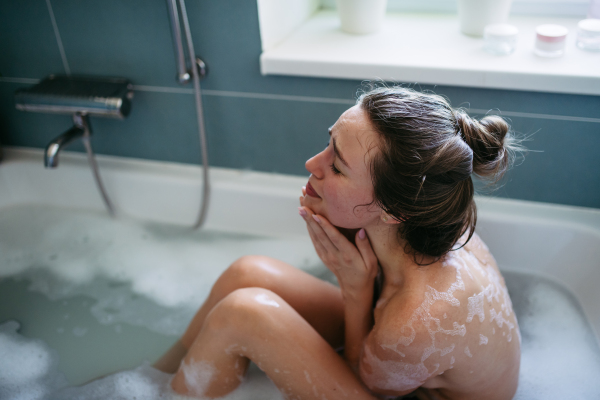 Crying woman in bathtub. Side view of young woman feeling depressed and lonely. Fertility problems, miscarriage.