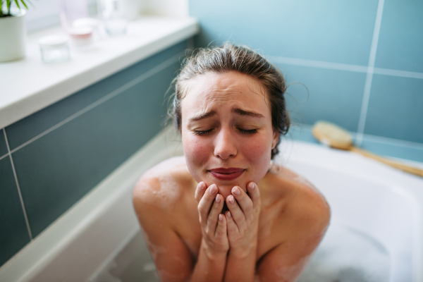 Crying, depressed woman in bathtub. Young woman feeling hopeless, having problems with harassment, rude comments in work.