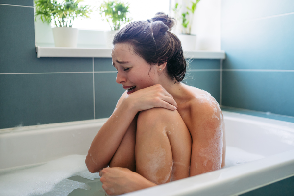 Crying woman in bathtub. Side view of young woman feeling depressed and lonely. Fertility problems, miscarriage.