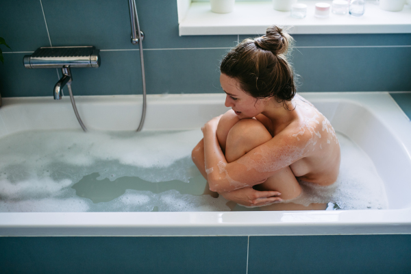 Desperate abused woman sitting in bathtub, crying and holding her body. Domestic violence and abuse, sexual harassment.