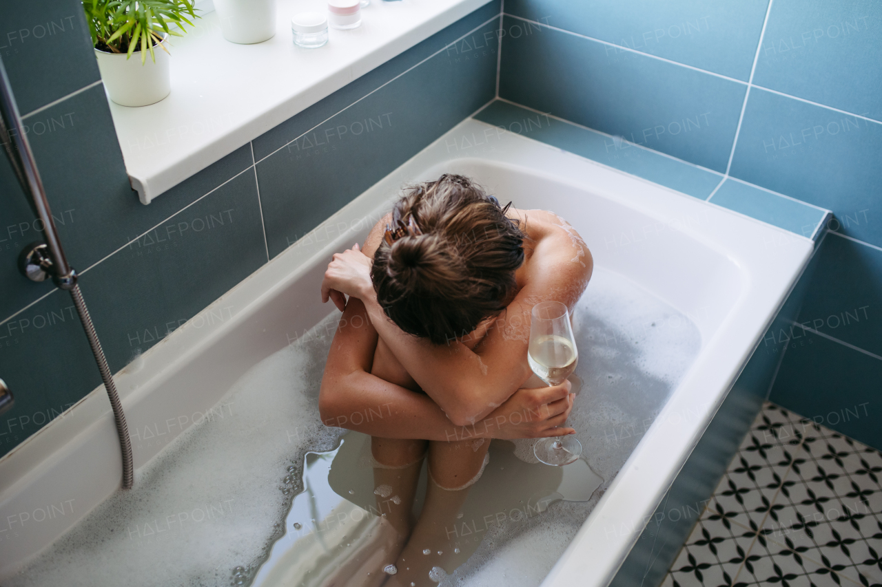 Depressed woman drinking wine in bathtub, is drunk. Young woman feeling hopeless, alcoholism issues in young age. Early alcohol abuse.